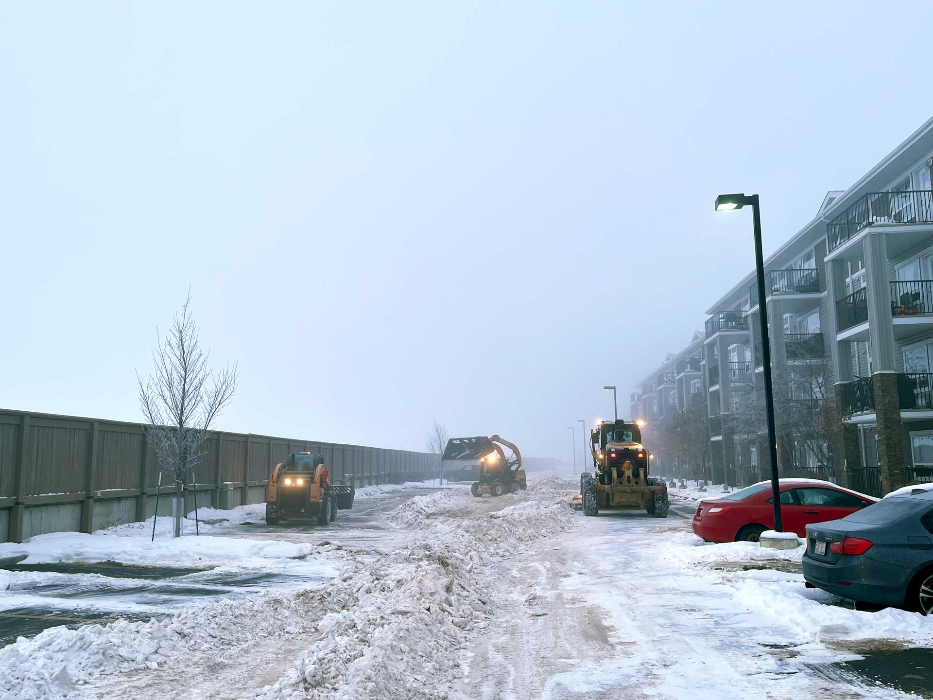 A motor snow grader, two skid steers and snow removal buckets parking lot condo complex Terwillegar.